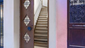 Una porta in legno con pannelli di vetro a forma di diamante, una scala che conduce a un piano superiore e un cancello decorativo in metallo.