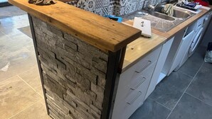 Uma cozinha com parede de pedra decorativa, bancada de madeira e pia embutida.