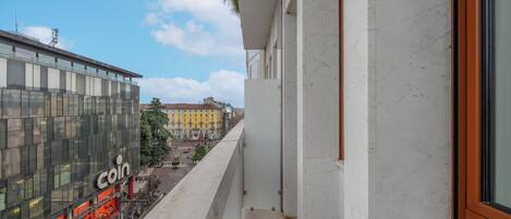 Un balcón con vista a un edificio moderno con el letrero 'Coin', un edificio amarillo al fondo y un cielo despejado.