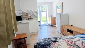 A room with a bed, a desk, a kitchenette, and a door leading to a balcony. - Cozy Studio in Hornchurch With Extra Bed (Hornchurch)