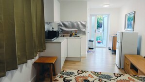 Una cocina compacta con microondas, pileta y alacenas. Hay una mesita de madera y un alfombra con diseño en el piso.