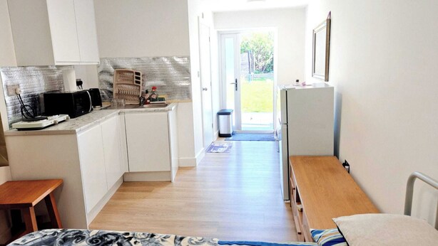 A compact room with a bed, a small table, a kitchenette with a microwave, and a view through a door. - Cozy Studio in Hornchurch With Extra Bed (Hornchurch)