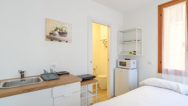 Una stanza compatta con angolo cottura, un letto, un forno a microonde e un piccolo frigorifero.