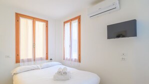Una camera da letto con un letto, due finestre con tende, un condizionatore d'aria e una televisione a parete.