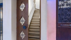 Una porta in legno con pannelli di vetro a forma di diamante, una scala che conduce a un piano superiore e un cancello decorativo in metallo.