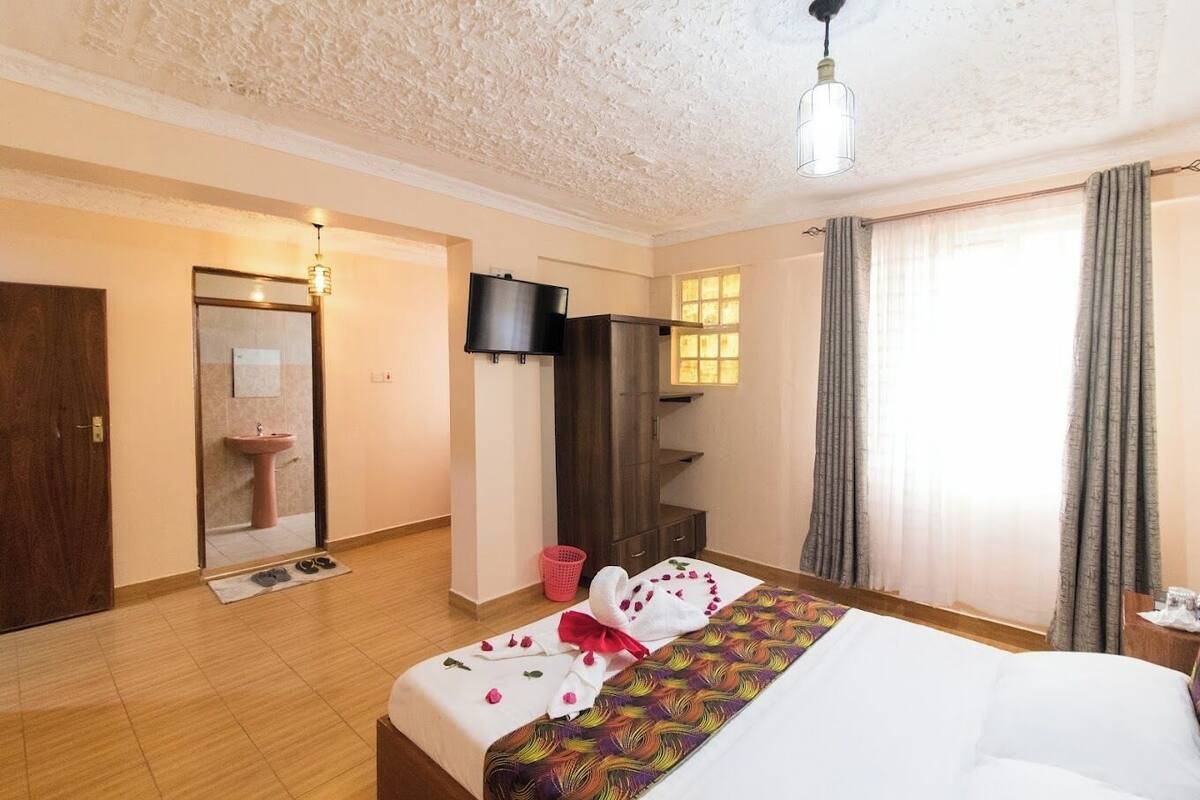 Une chambre d’hôtel comprenant un lit, une télévision, une armoire, une salle de bain et une fenêtre avec des rideaux.