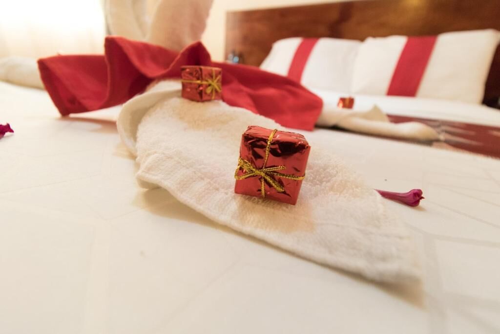 A neatly made bed with a white comforter and red pillows. Two small red gift boxes are placed on the bed.
