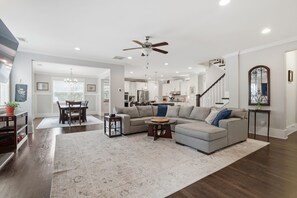 Ein geräumiges Wohnzimmer mit einer großen Eckcouch, einem Essbereich mit Tisch und Stühlen, einer Küche im Hintergrund und einer Treppe, die zu einer oberen Ebene führt.