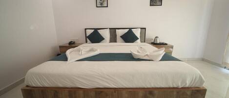 A neatly made bed with a wooden headboard, white bedding, and two pillows. There are two bedside tables with lamps and a small clock.
