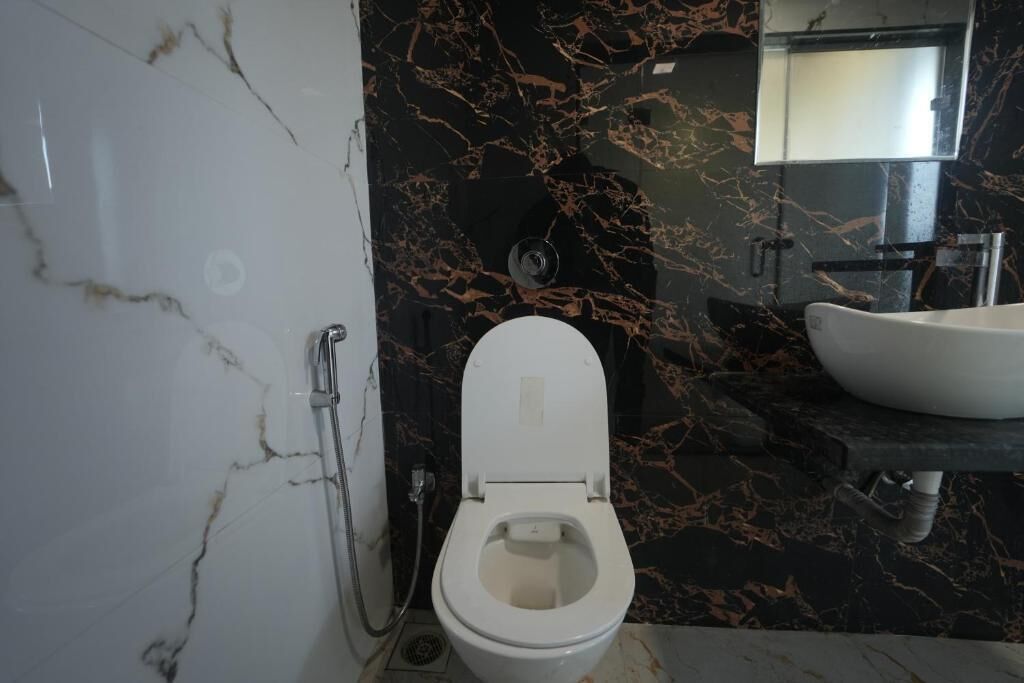 A bathroom with a white toilet, a sink, and a marble backsplash.