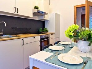 A modern kitchen with white cabinets, a black countertop, and a dining area set with plates, cutlery, and a vase of flowers. - Il Trio, smart stay Bocconi (Milano)