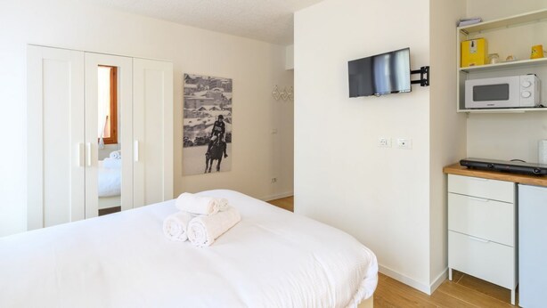 Une chambre avec un lit, un téléviseur fixé au mur, un four à micro-ondes et une petite kitchenette.