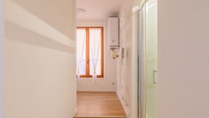 Un couloir étroit avec un plancher en bois, un radiateur et une fenêtre avec des rideaux.