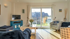 En moderne stue med et fladskærms-tv, et blåt skab, et glasbord og to ternede lænestole.