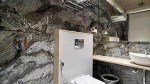 Une salle de bain moderne avec un mur en marbre, des toilettes blanches, un lavabo et une douche.