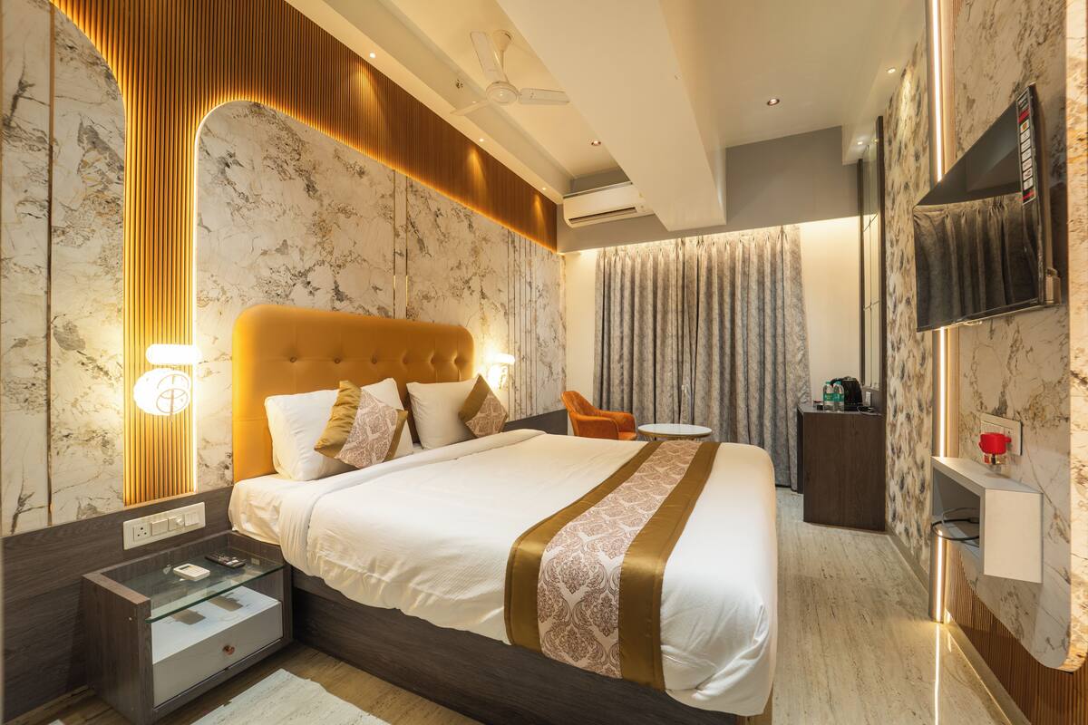 A modern hotel room with a large bed, a bedside table, a small desk, a chair, a TV, and an air conditioning unit.