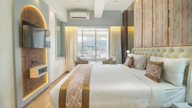 Une chambre d’hôtel moderne dotée d’un grand lit, d’un téléviseur à écran plat fixé au mur, d’un coin salon avec des fauteuils et d’une grande fenêtre avec des rideaux.