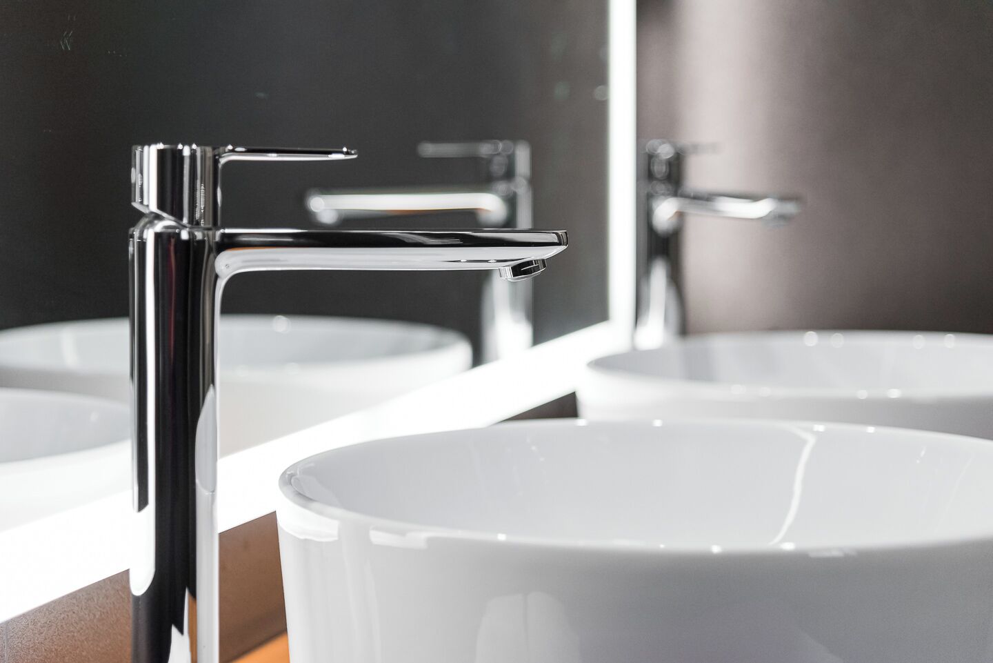 Ein modernes Badezimmer mit Chromarmaturen, weißen Waschbecken und einem Spiegel, der den Raum widerspiegelt.