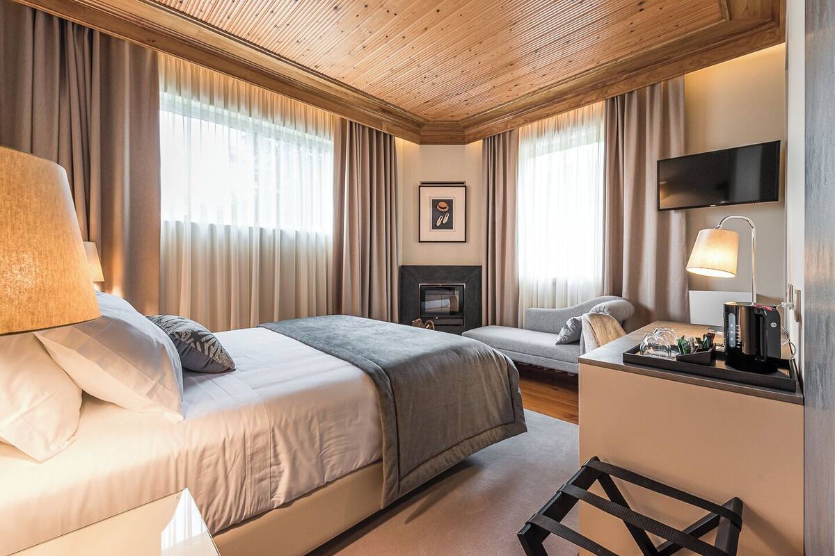 Ein Hotelzimmer mit Holzboden, zwei Betten, einem Fernseher, einem Schreibtisch mit Lampe und einem Kamin.