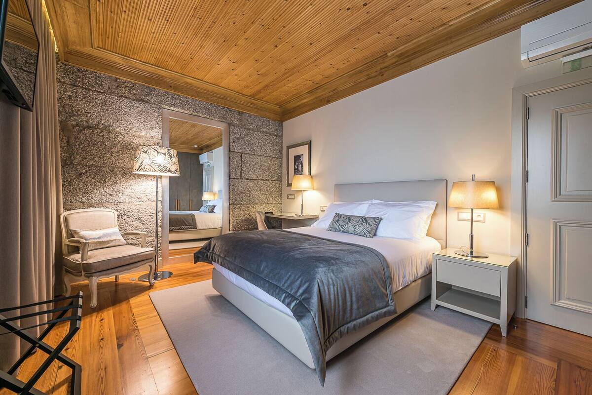 Ein Schlafzimmer mit einem Bett, Nachttischen, einem Sessel, einem Spiegel und einer Steinwand.