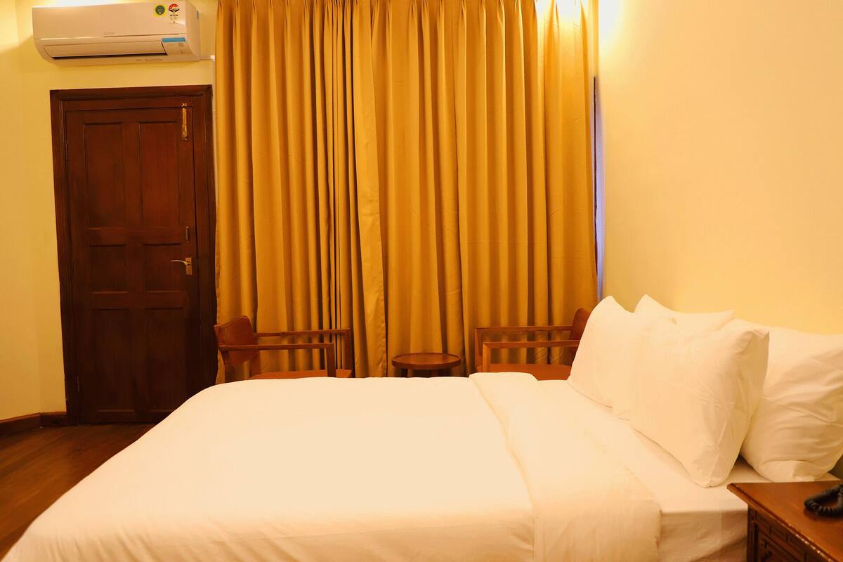 A hotel room with a bed, a wooden door, a small table, and a chair.