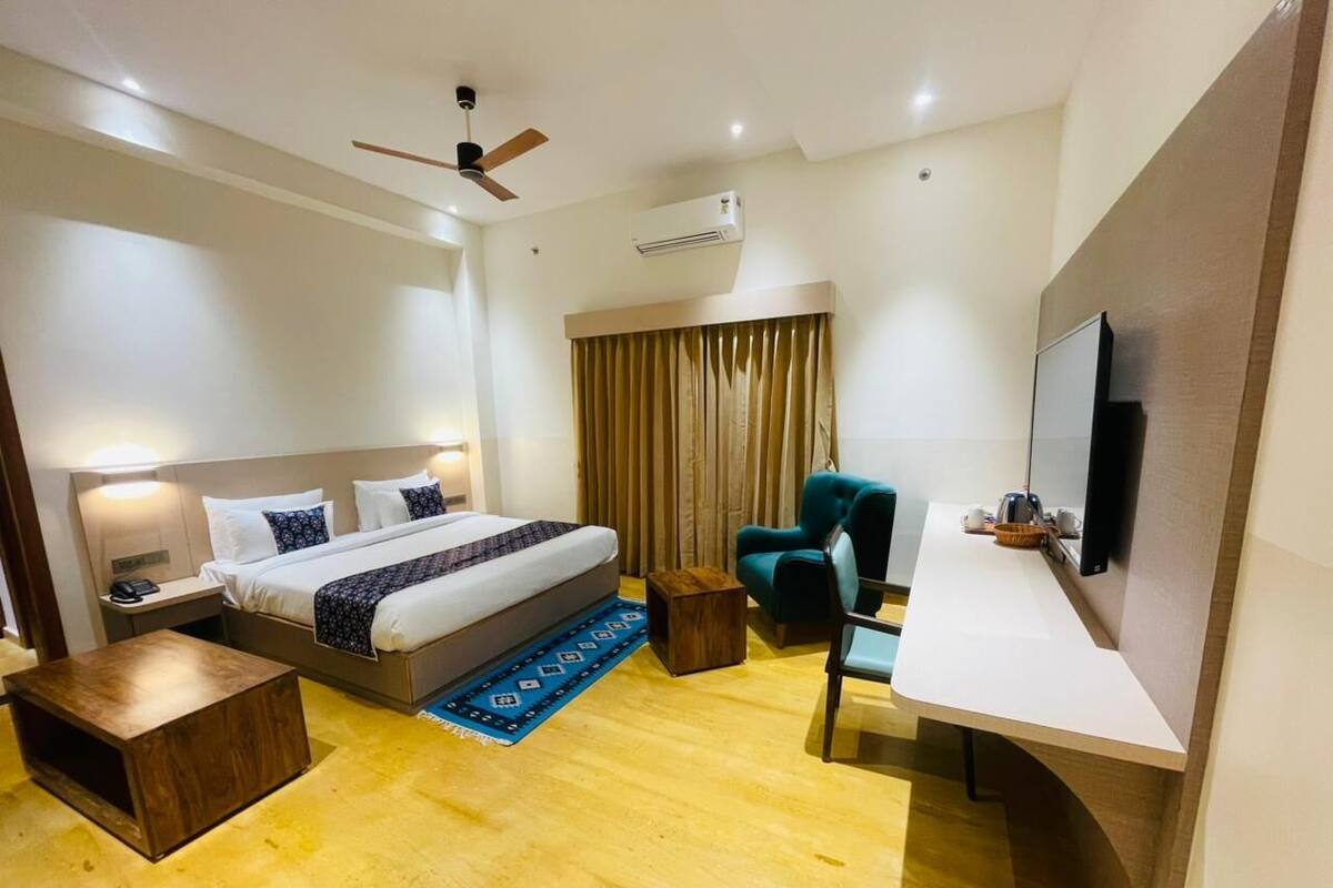 A hotel room with a bed, bedside table, chair, desk, and a TV.