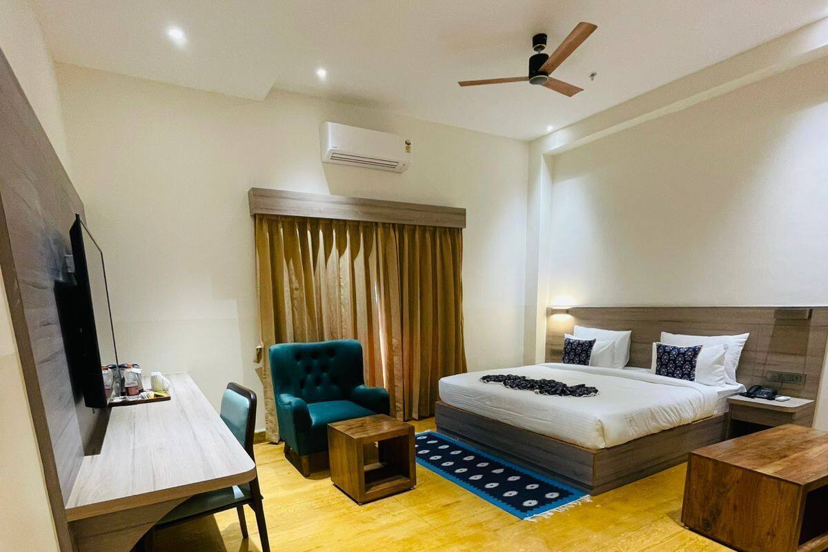 A hotel room with a bed, a desk, a chair, a TV, and a ceiling fan.