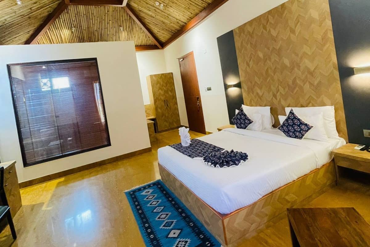 A bedroom with a large bed, a wooden ceiling, a large window, and a blue patterned rug.