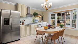 A kitchen with a stainless steel refrigerator, a built-in oven, a sink, and a dining area with a table and chairs. - Modern 4BR Retreat - Fully Equipped - Near Disney (Chino)