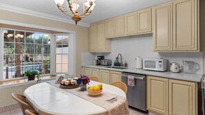 A kitchen with a dining area, featuring a large window, a chandelier, and various kitchen appliances. - Modern 4BR Retreat - Fully Equipped - Near Disney (Chino)