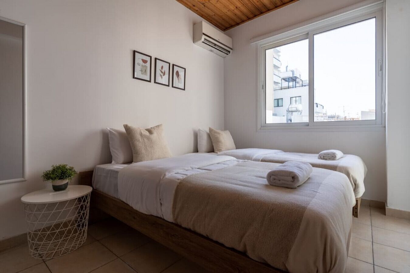 Una camera da letto con due letti, un piccolo tavolo rotondo con una pianta e una finestra con vista sulla città.