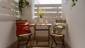 Ein kleiner Balkon mit einem Holztisch, zwei Stühlen, einem roten Kissen, einem weißen Kissen und einem Blumentopf.
