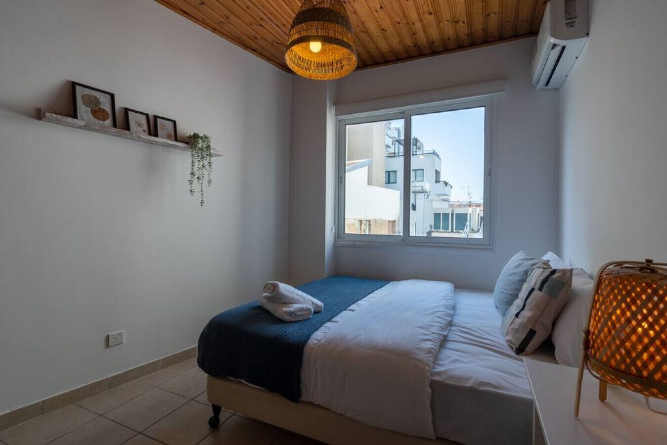 A bedroom with a bed, a window, a hanging light fixture, and a wall-mounted air conditioner.