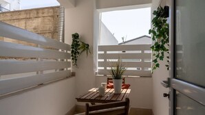 Ein kleiner Balkon mit Holztisch, Blumentopf und weißer Umzäunung.