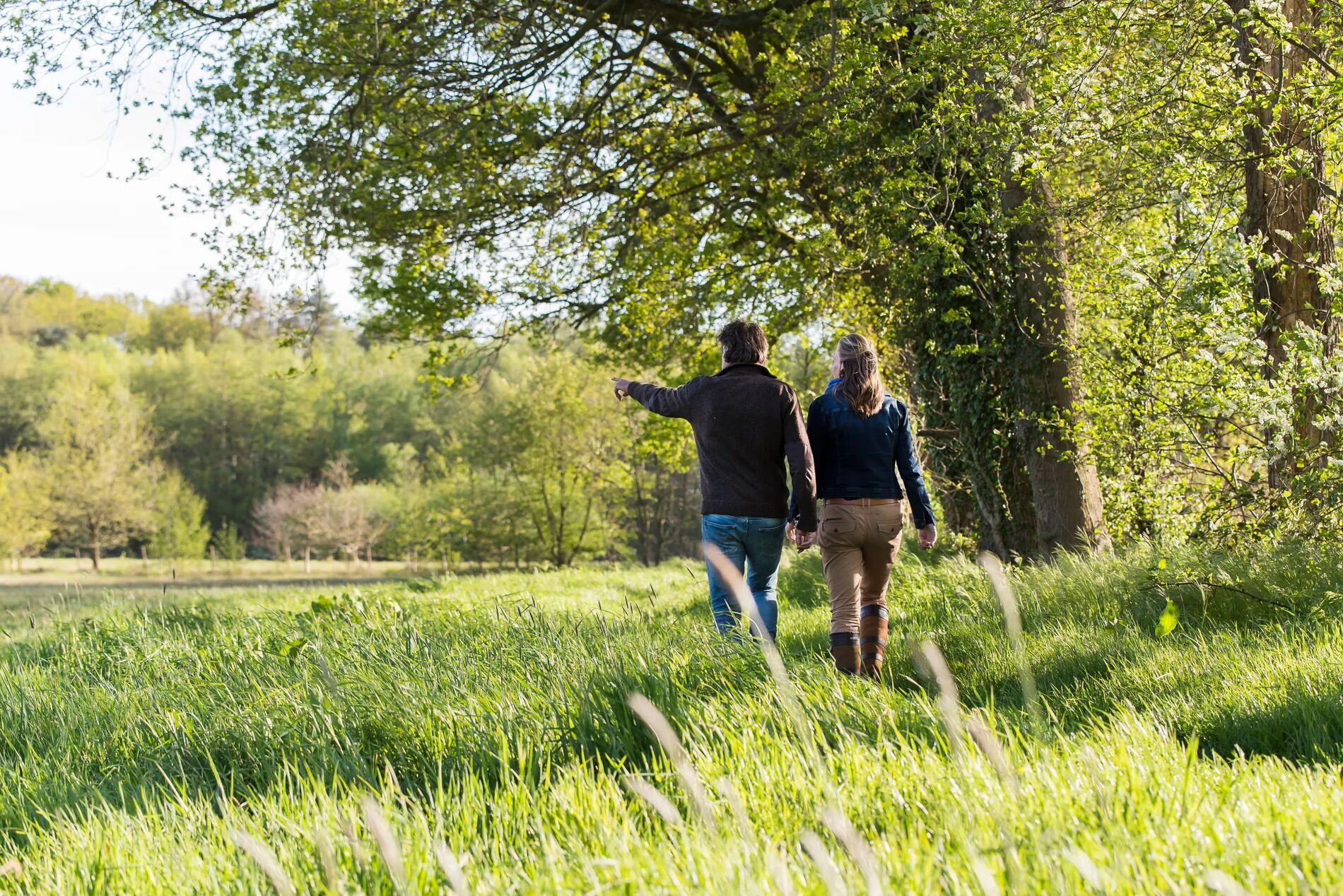 A couple walking in a grassy field with trees in the background.