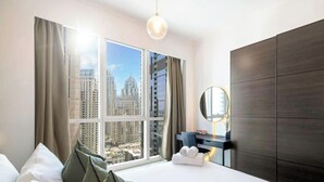 A hotel room with a large window, a bed, a bedside table with a lamp, and a dark wood wardrobe. - LUX The Dubai Marina View Suite (Dubai)