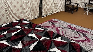 Een kamer met een groot bed, twee houten stoelen en een kamer met een patroon gordijn.