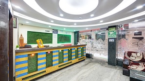 Un espace d’accueil au design moderne, comprenant un comptoir aux motifs rayés verts et bleus, une petite plante et un objet décoratif. Des panneaux indiquent l’emplacement d’un poste de travail et la sortie.