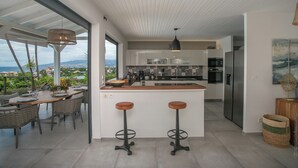 Een moderne keuken met een groot eiland, barstoelen en uitzicht op zee.