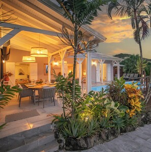 An outdoor dining area with a pool, surrounded by tropical plants and a covered patio. - Villa Perlane Bay - Luxury villa, 5 bedrooms, heated pool, Caribbean sea view (Les Trois-Îlets)