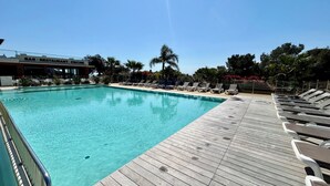 A swimming pool with a wooden deck and lounge chairs, surrounded by palm trees and a bar/restaurant. - Luxury mobile home sea view Domaine de l'Ile d'Or Saint Raphaël (Saint-Raphaël)