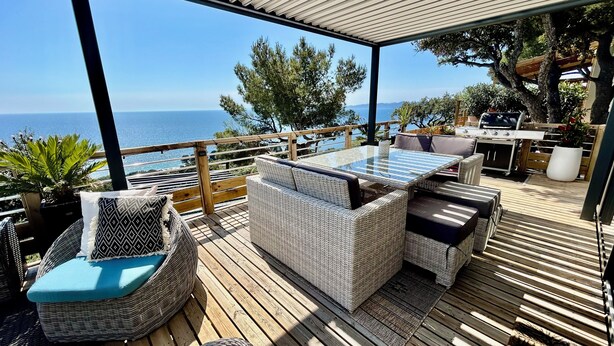 A covered outdoor seating area with wicker furniture, a glass-top table, and a view of the sea. - Luxury mobile home sea view Domaine de l'Ile d'Or Saint Raphaël (Saint-Raphaël)