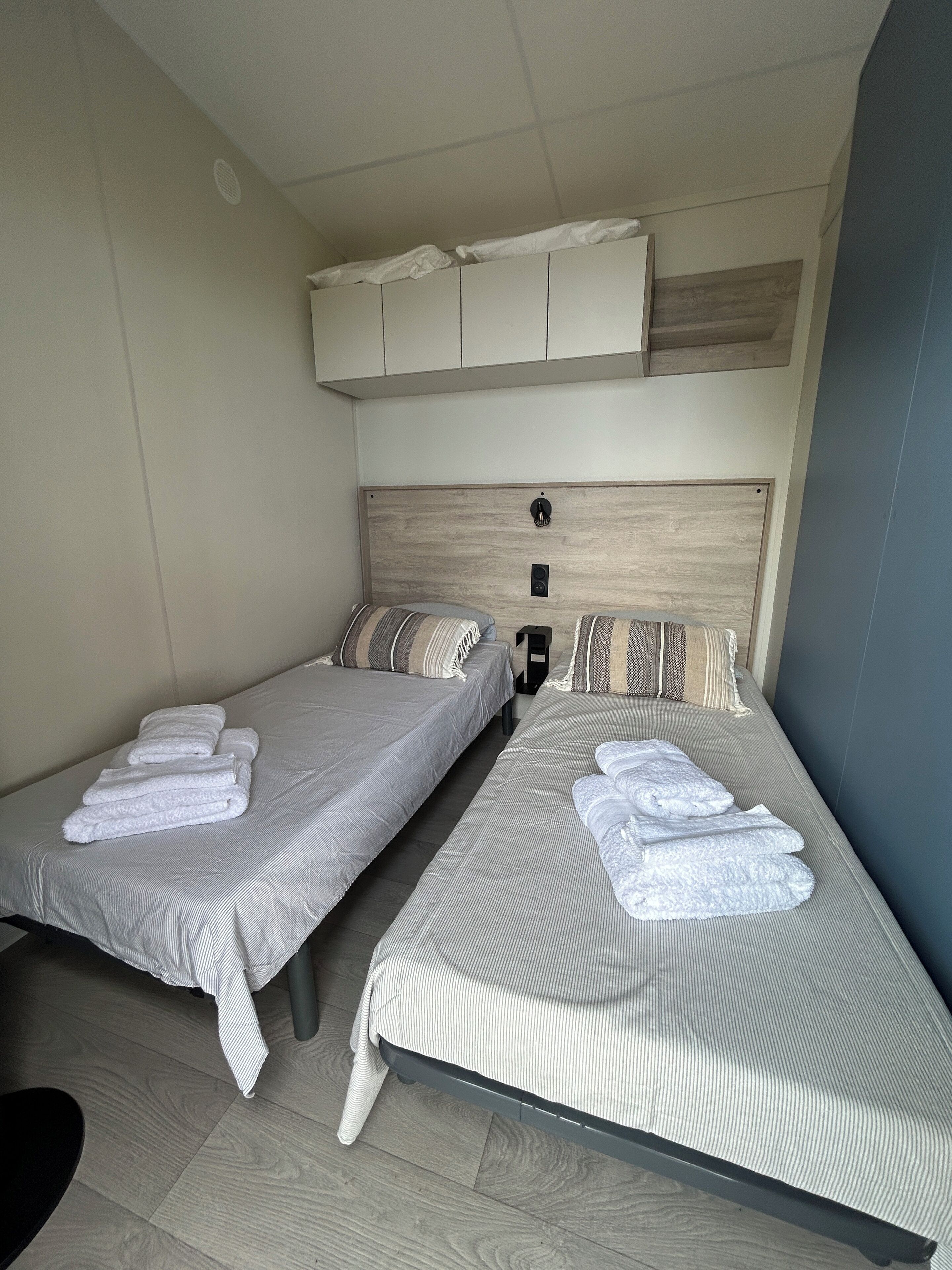 Two single beds with white linens and striped bedding, a wooden headboard, and a ceiling vent.