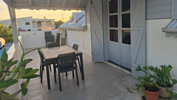 Une terrasse couverte avec une table et des chaises, des plantes en pot et une porte coulissante.