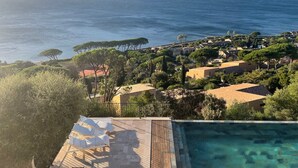 En semesteranläggning vid kusten med en pool, solstolar och utsikt över havet.
