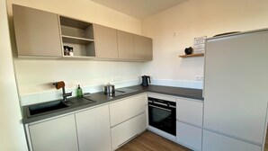 Moderni keittiö, jossa on valkoiset kaapit, musta työtaso, sisäänrakennettu uuni ja jääkaappi.