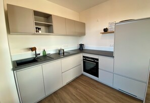 A modern kitchen with white cabinetry, a black countertop, a built-in oven, and a refrigerator. - Relaxation at the foot of the Swabian Alb | Cozy apartment in Weilheim / Teck (Weilheim an der Teck)