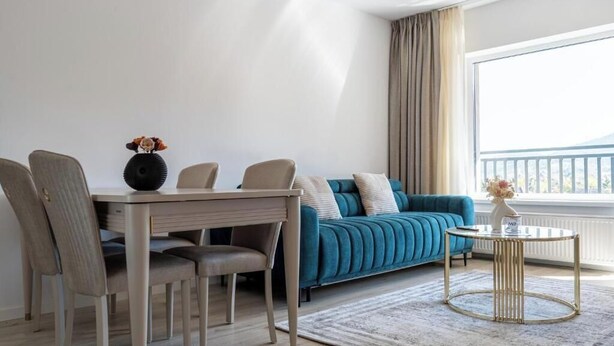 A modern living room with a sofa, dining table, chairs, and a small round table with a vase. - Nest & Rest Brasov - Cozy Apartment (Brasov)