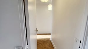 Un corridoio con pareti bianche e pavimento in legno, che conduce a una stanza con una lampada a soffitto.