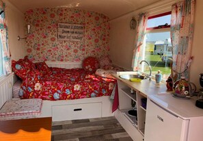 A cozy bedroom with a floral bedspread, a small kitchenette with a sink, and a window with curtains.